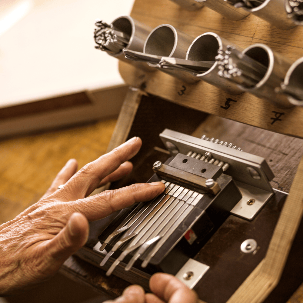 Hand tuning a kalimba with metal tines, wooden body, and numbered tone pipes for precise musical calibration.