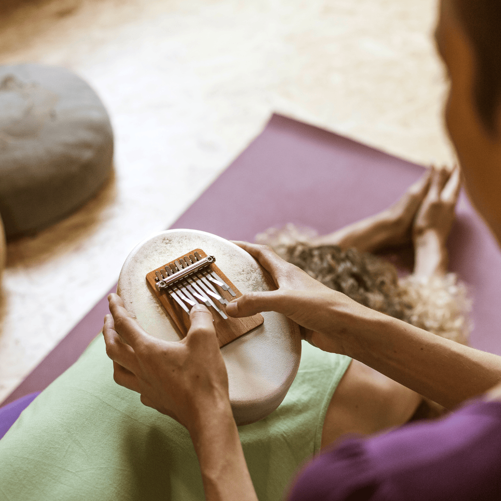 Person playing kalimba on yoga mat, relaxing with healing musical instrument