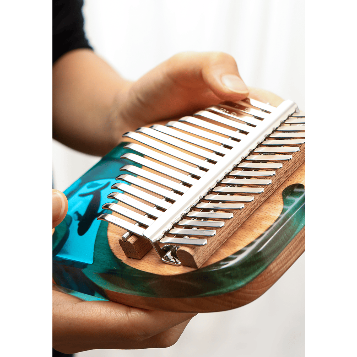 Hand playing blue and green kalimba with wooden body and metal tines, healing musical instrument