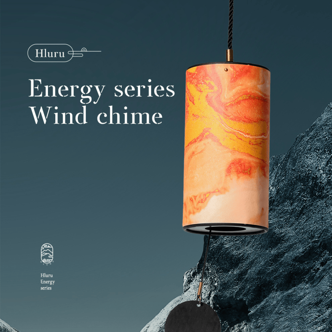 Hluru Energy series wind chime with vibrant orange swirls, hanging near rocky terrain for serene ambiance.