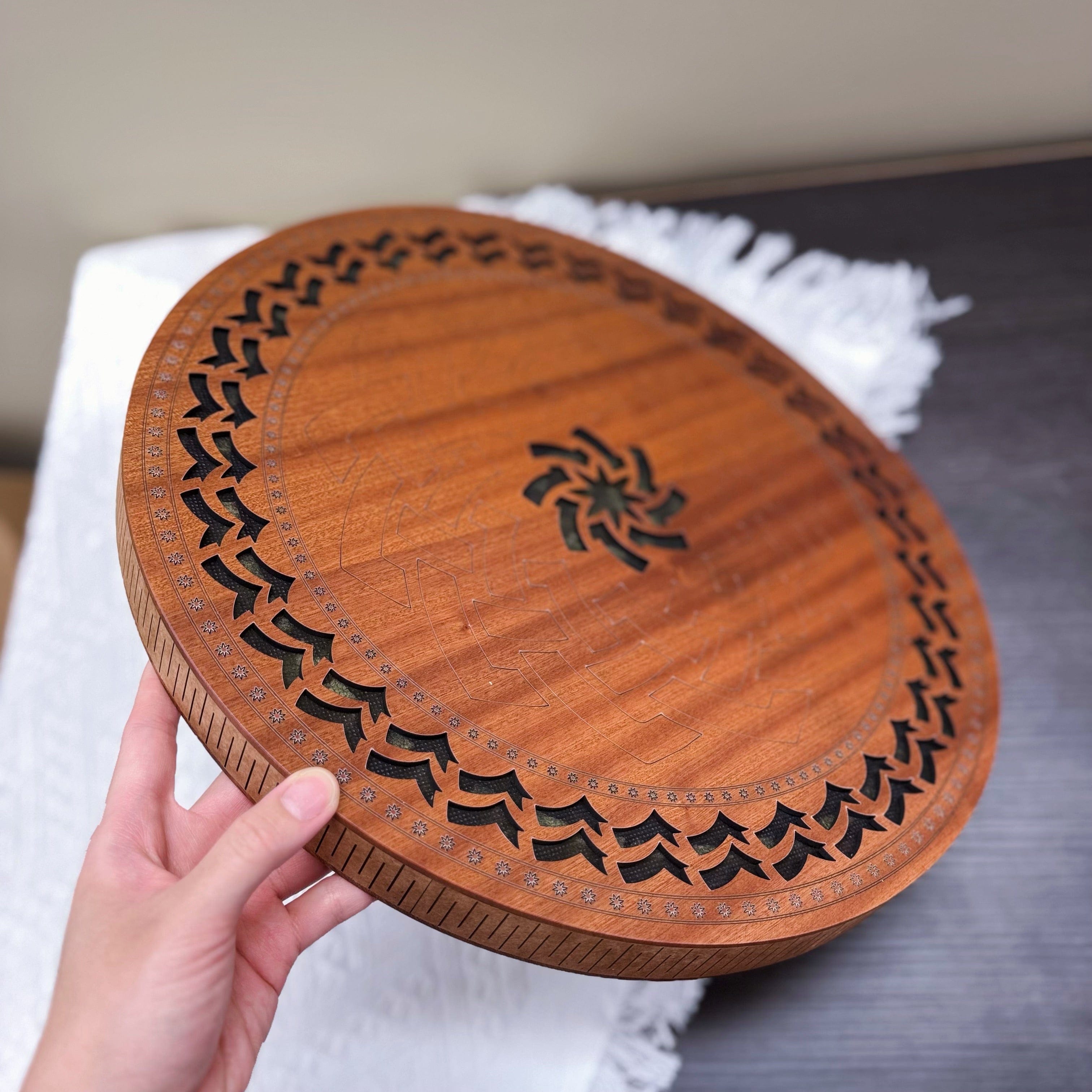 Hand holding a wooden tongue drum with carved tree and sun designs, ideal for meditation and healing sound therapy.