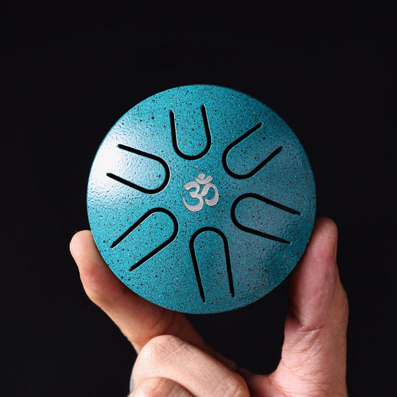 Teal tongue drum with Om symbol, held in hand against black background — healing musical instrument
