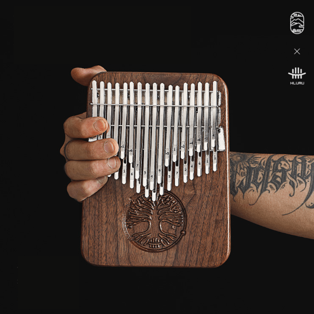 Hand holding wooden kalimba with tree of life design, metal tines numbered for easy play