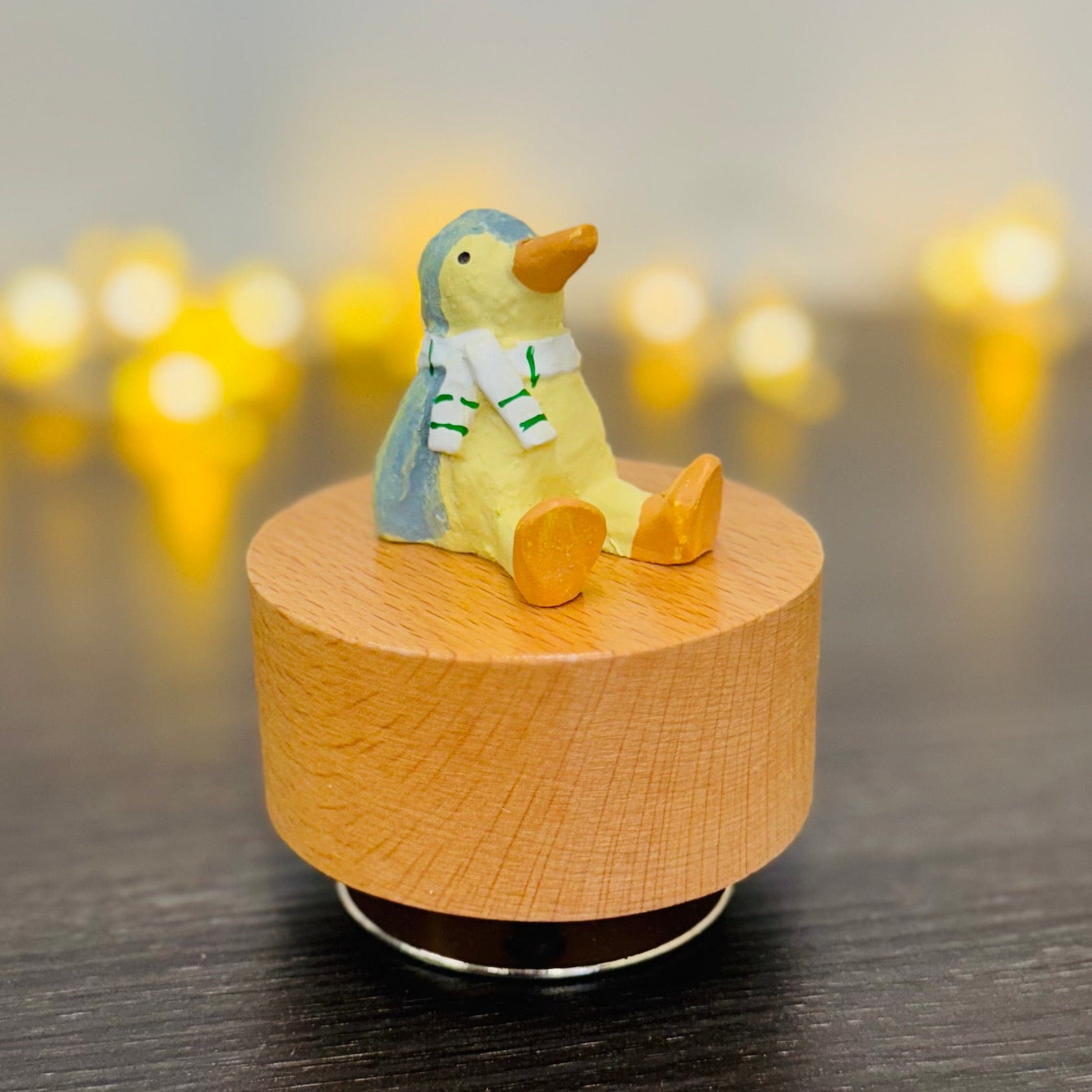 Charming penguin figurine on wooden music box with cozy scarf, warm bokeh lights background