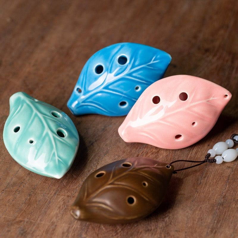 Leaf-shaped ceramic ocarinas in blue, pink, green, and brown on wood — soothing musical instruments for mindfulness