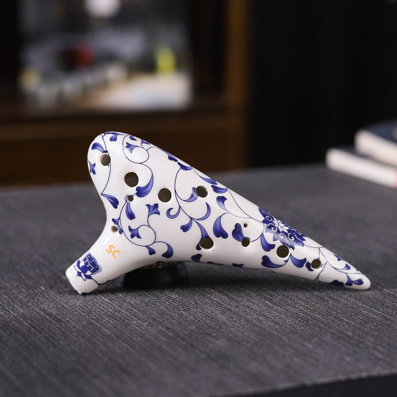 Blue and white ceramic ocarina with floral patterns, resting on gray fabric surface