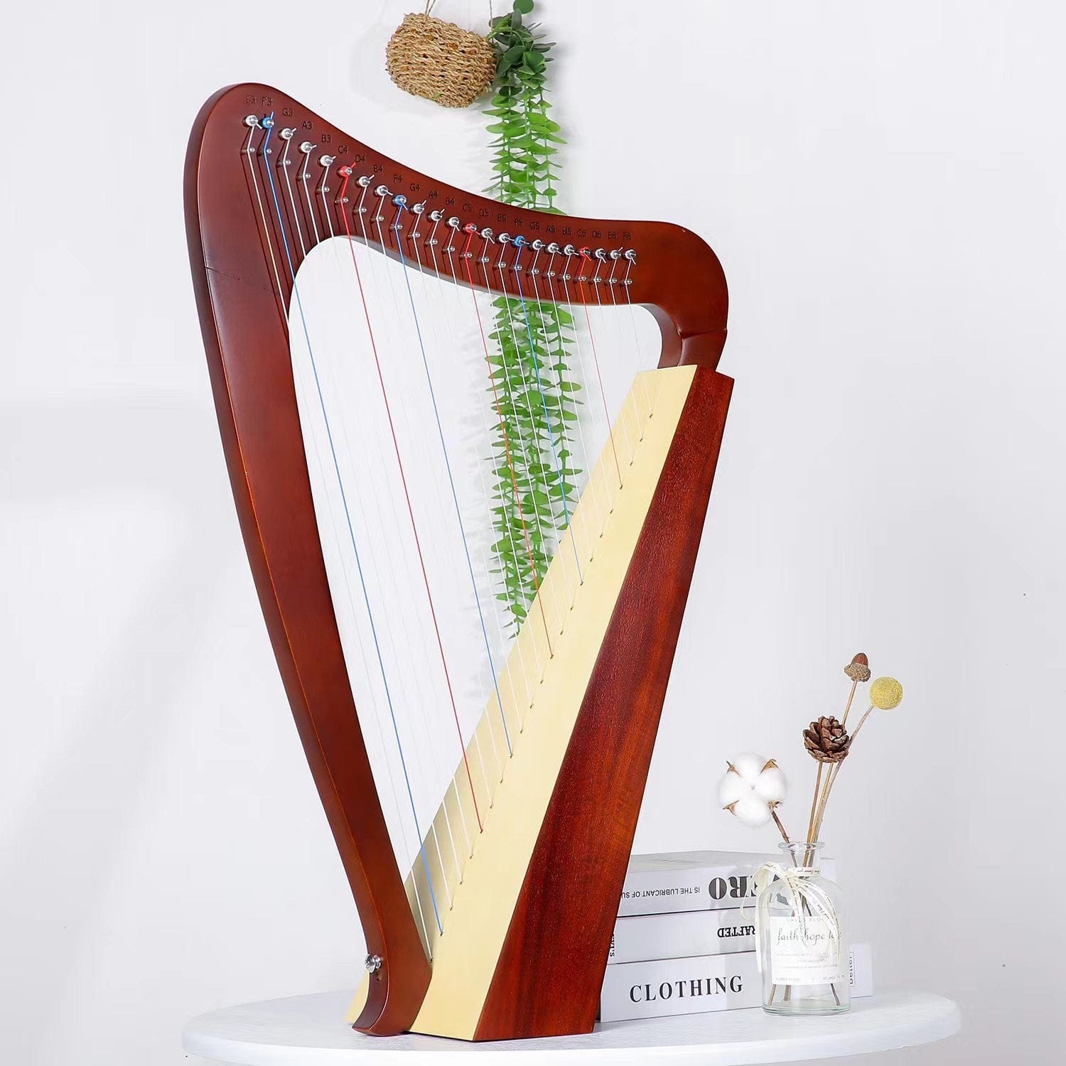 Wooden lyre harp with colorful strings, displayed on white table with greenery and decor, ideal for healing music and relaxation