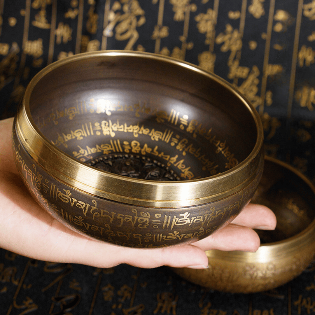 Hand holding brass singing bowl with Tibetan script, ideal for meditation and healing sound therapy