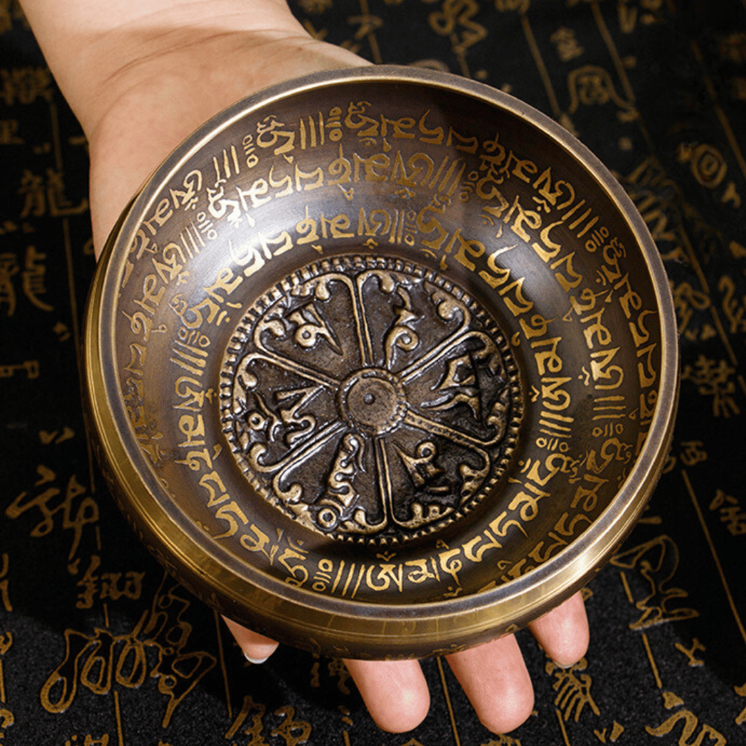 Hand holding ornate singing bowl with Tibetan script and Dharma wheel design for meditation and healing sound