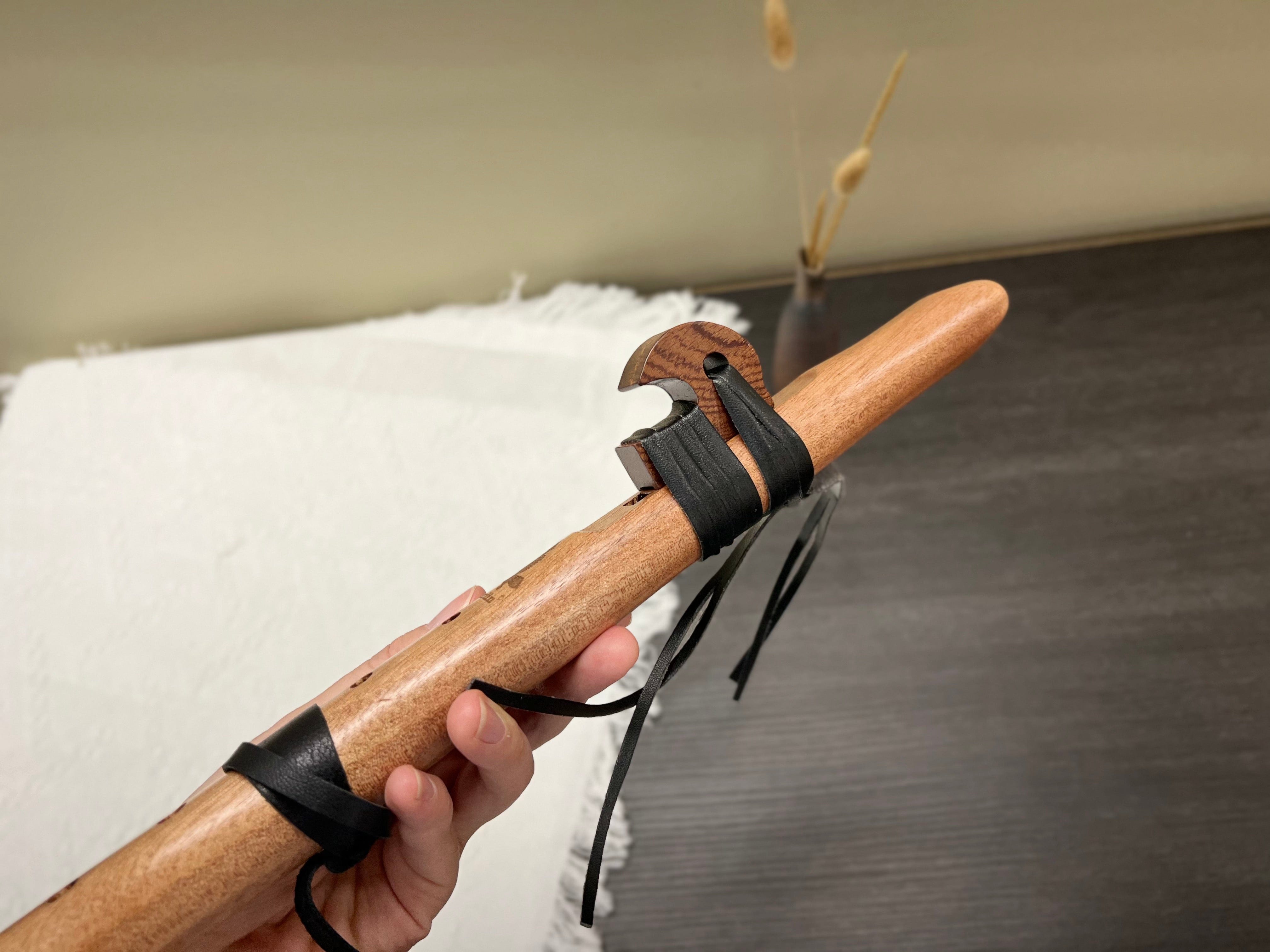 Hand holding wooden flute with black leather straps, showcasing its craftsmanship and design.