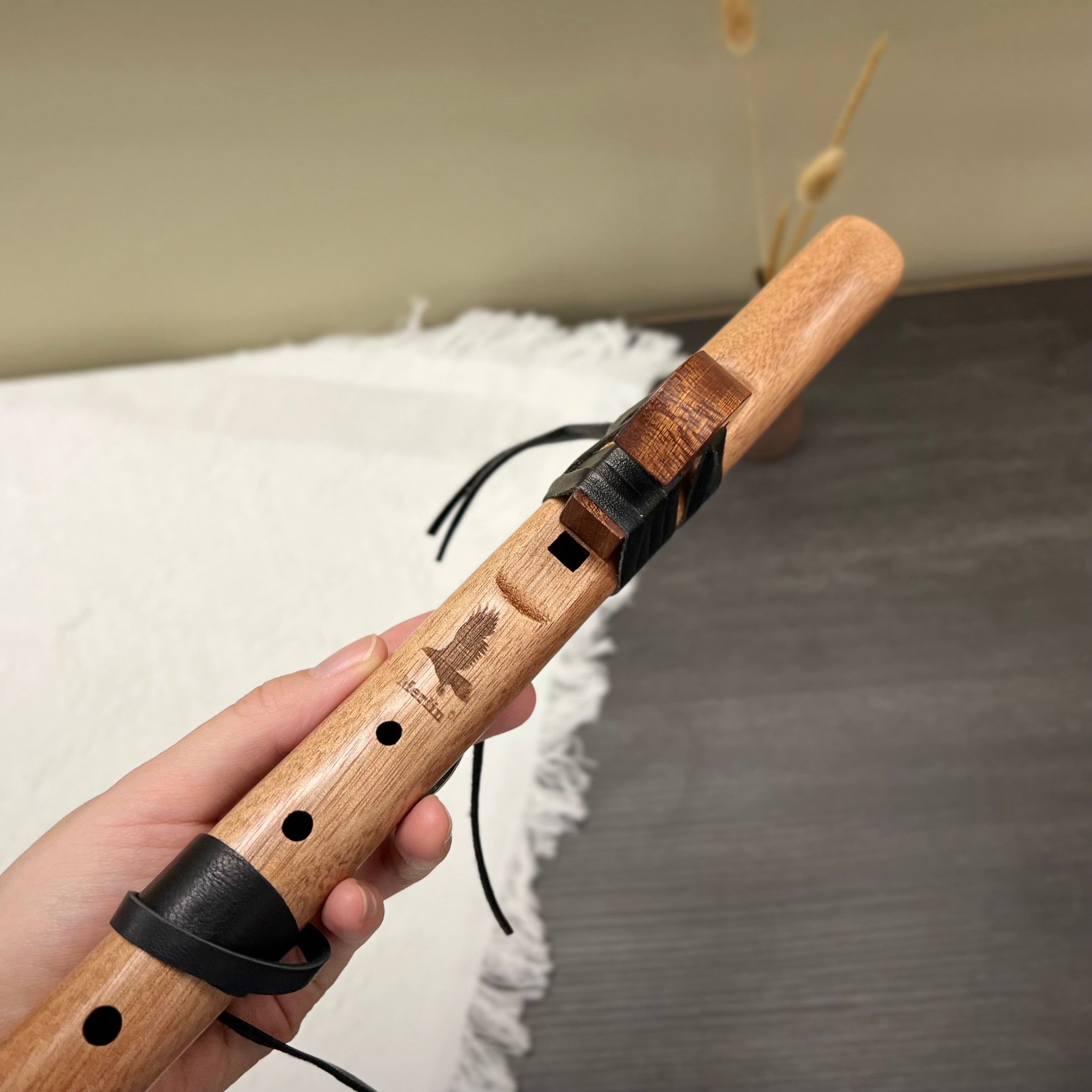 Hand holding wooden flute with leather wrap and bird engraving, ideal for healing music and relaxation.