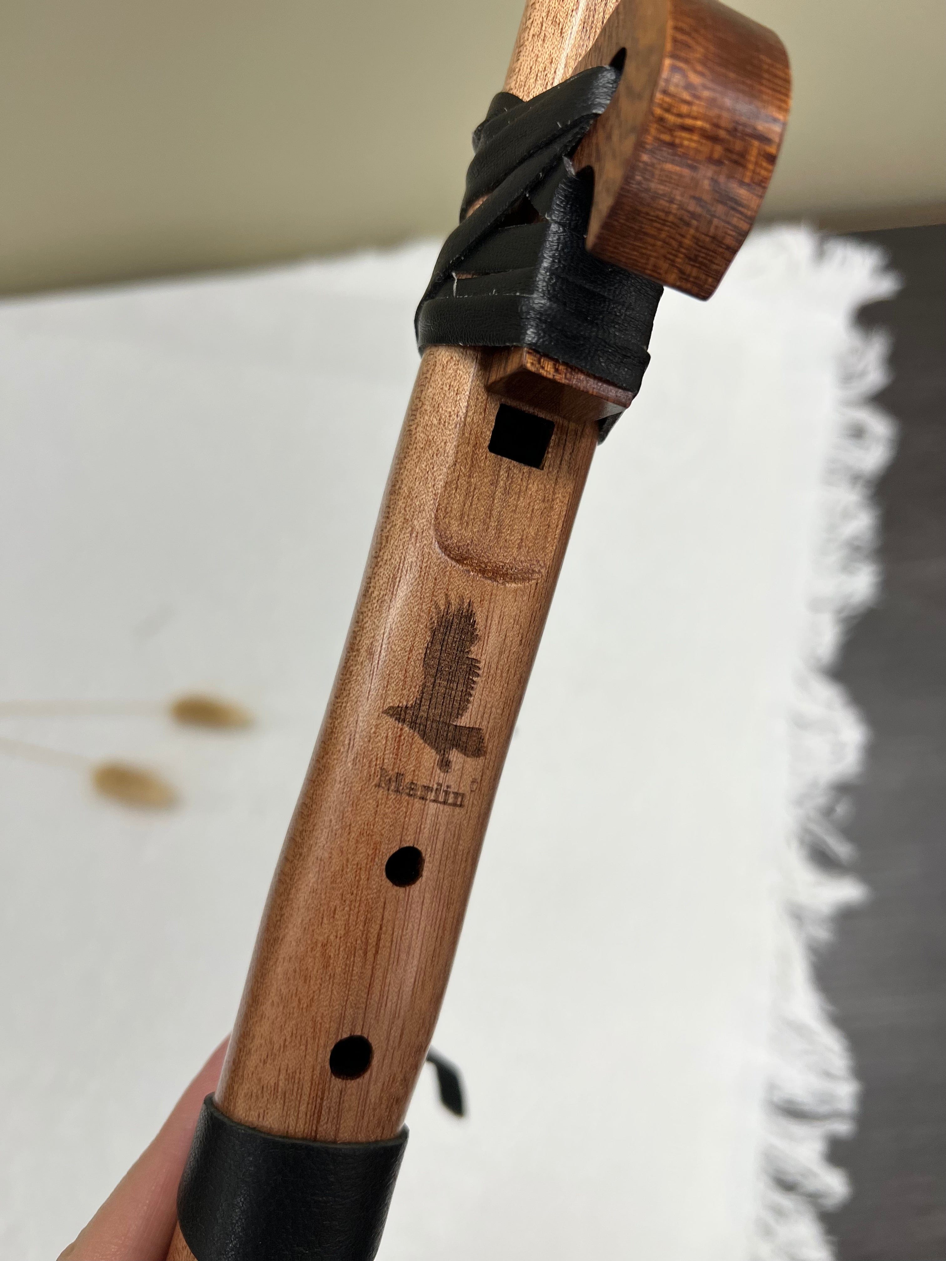 Merlin wooden flute with engraved bird, black leather straps, and rich wood grain for healing music