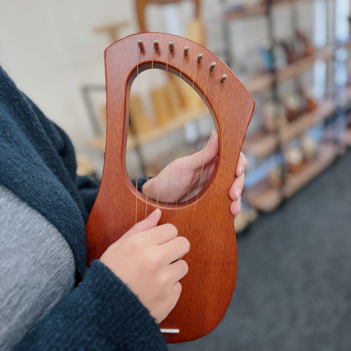 Hand playing a wooden lyre harp, showcasing its strings and curved design for healing music.