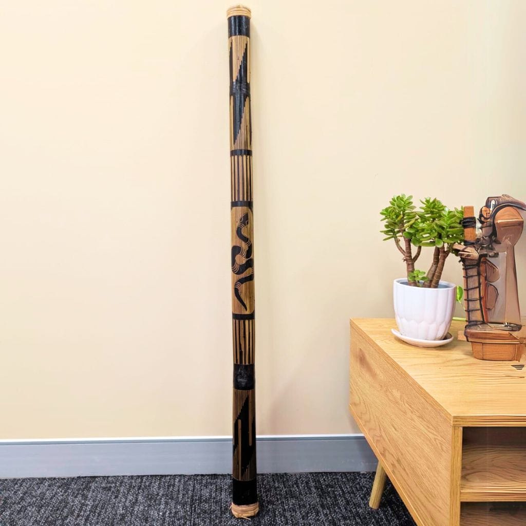 Handcrafted didgeridoo with black and natural wood patterns, standing beside wooden table with succulent plant