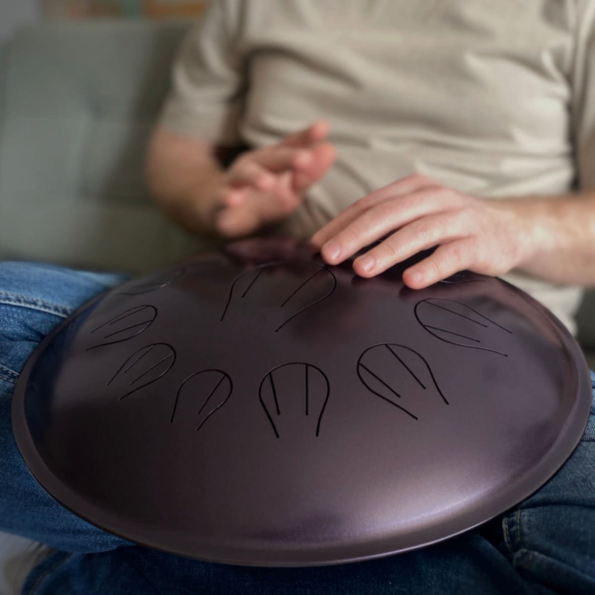 Person playing a dark handpan drum on lap, relaxing at home with healing musical instrument