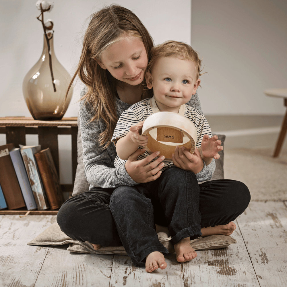 Child and sibling playing wooden kalimba together, cozy home setting with books and decor