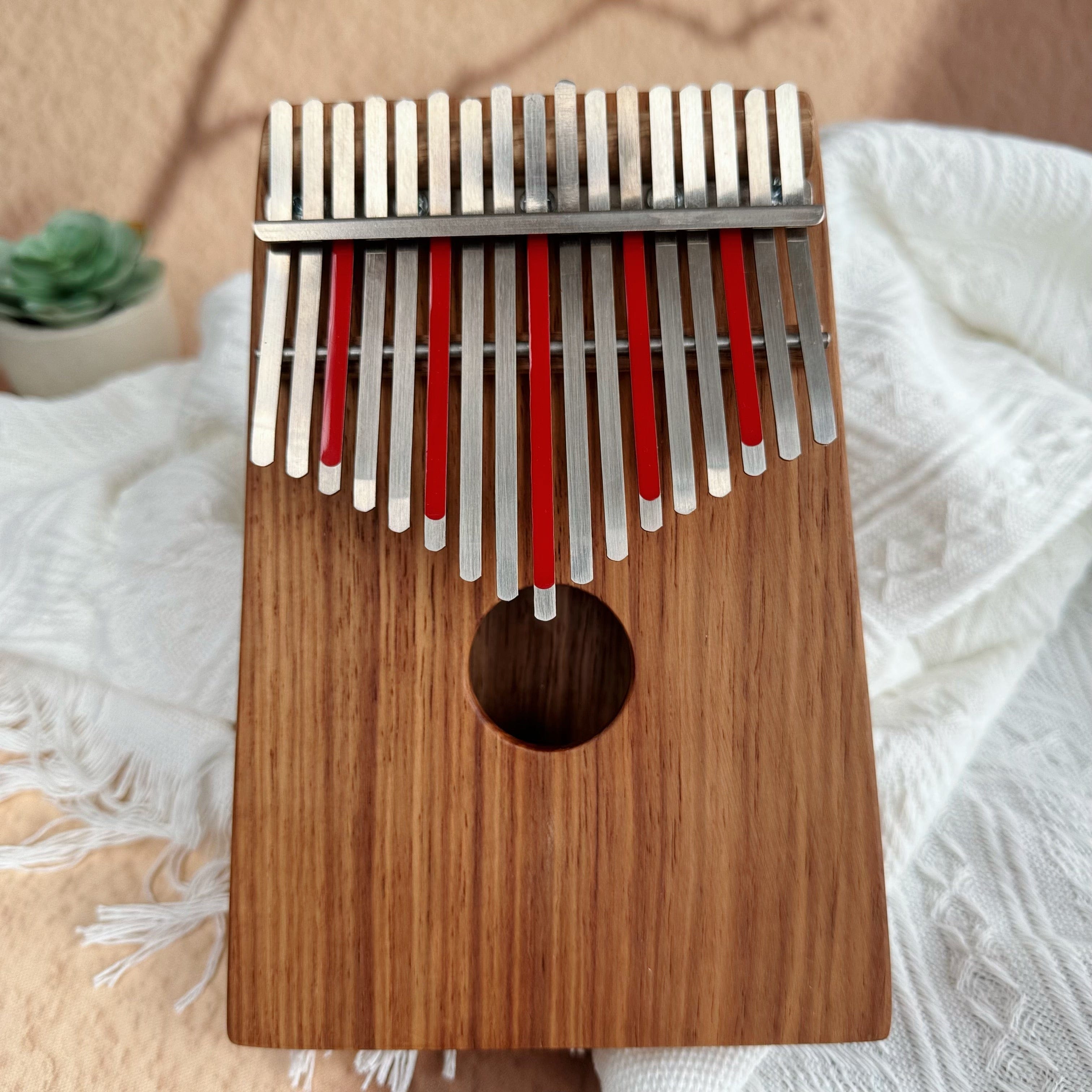 Wooden kalimba with red-tipped metal tines, resting on white fabric beside a succulent plant.