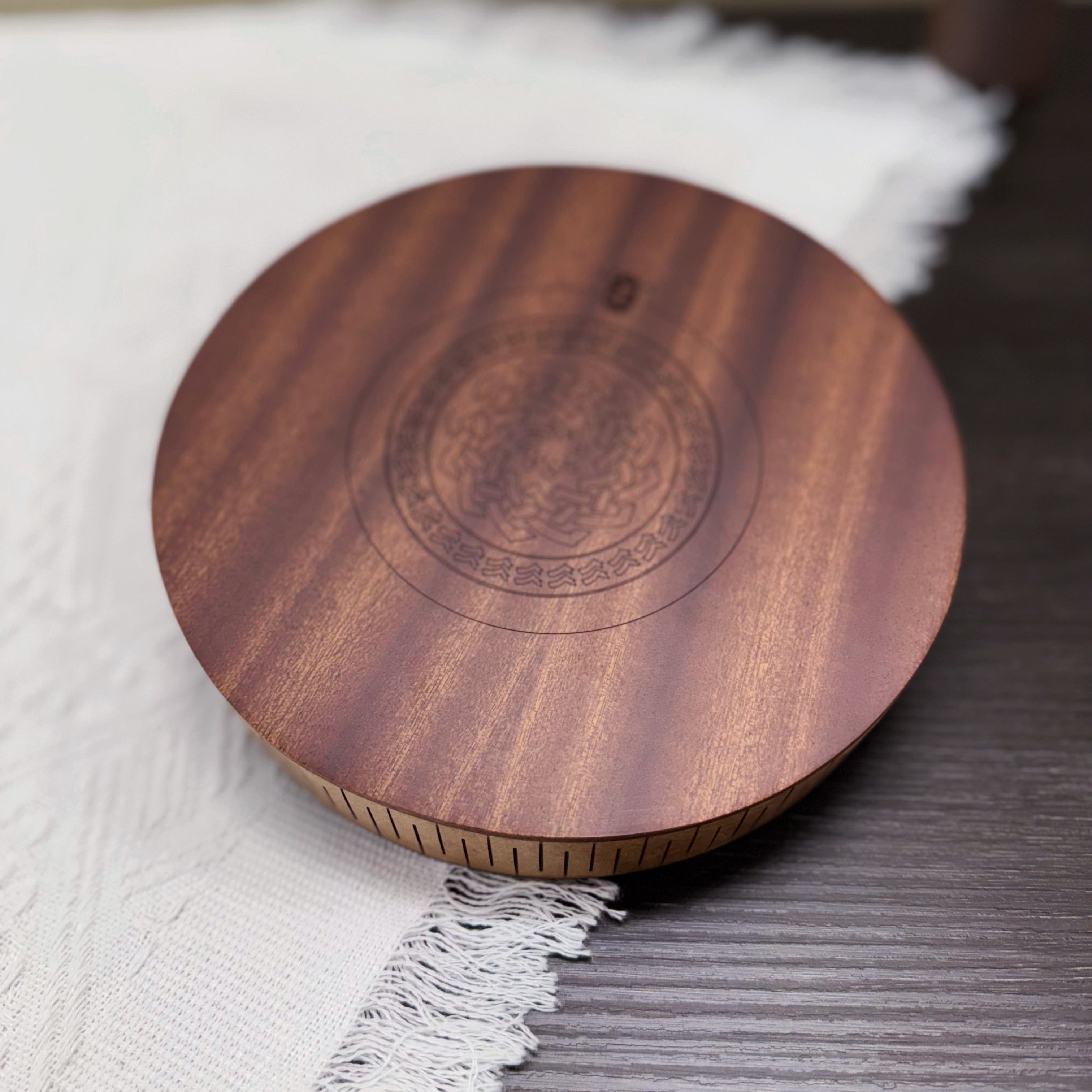 Handcrafted wooden tongue drum with engraved mandala design, resting on white fabric