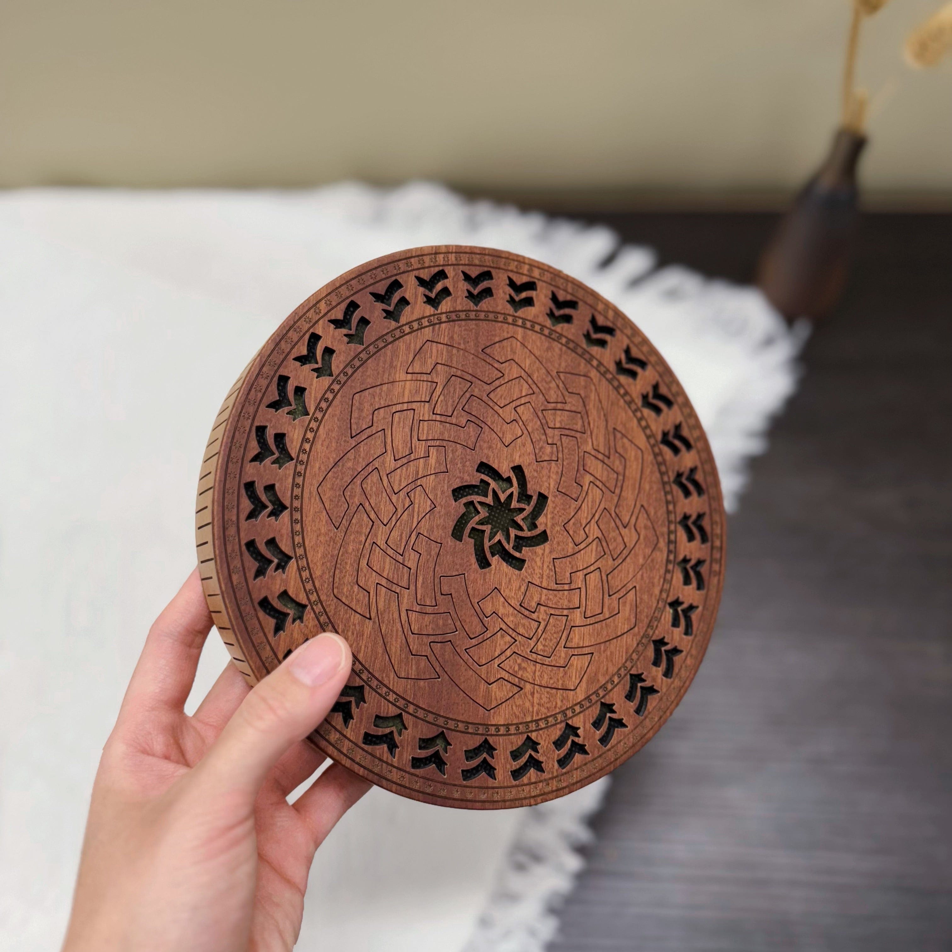 Hand holding intricately carved wooden tongue drum with geometric patterns, ideal for meditation and healing sound therapy.