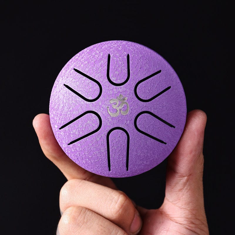 Purple tongue drum with Om symbol, held in hand against black background — healing musical instrument