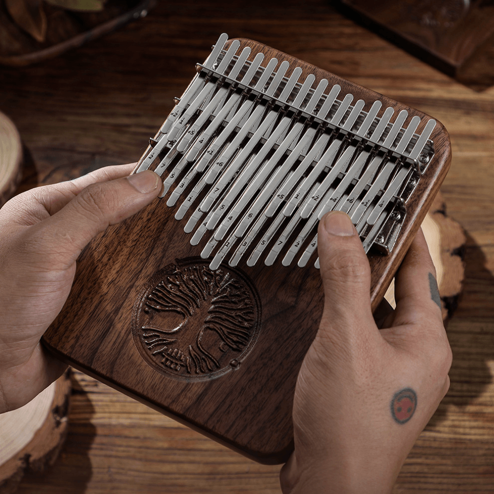 Hand holding wooden kalimba with metal tines and tree of life carving, ideal for healing music and meditation