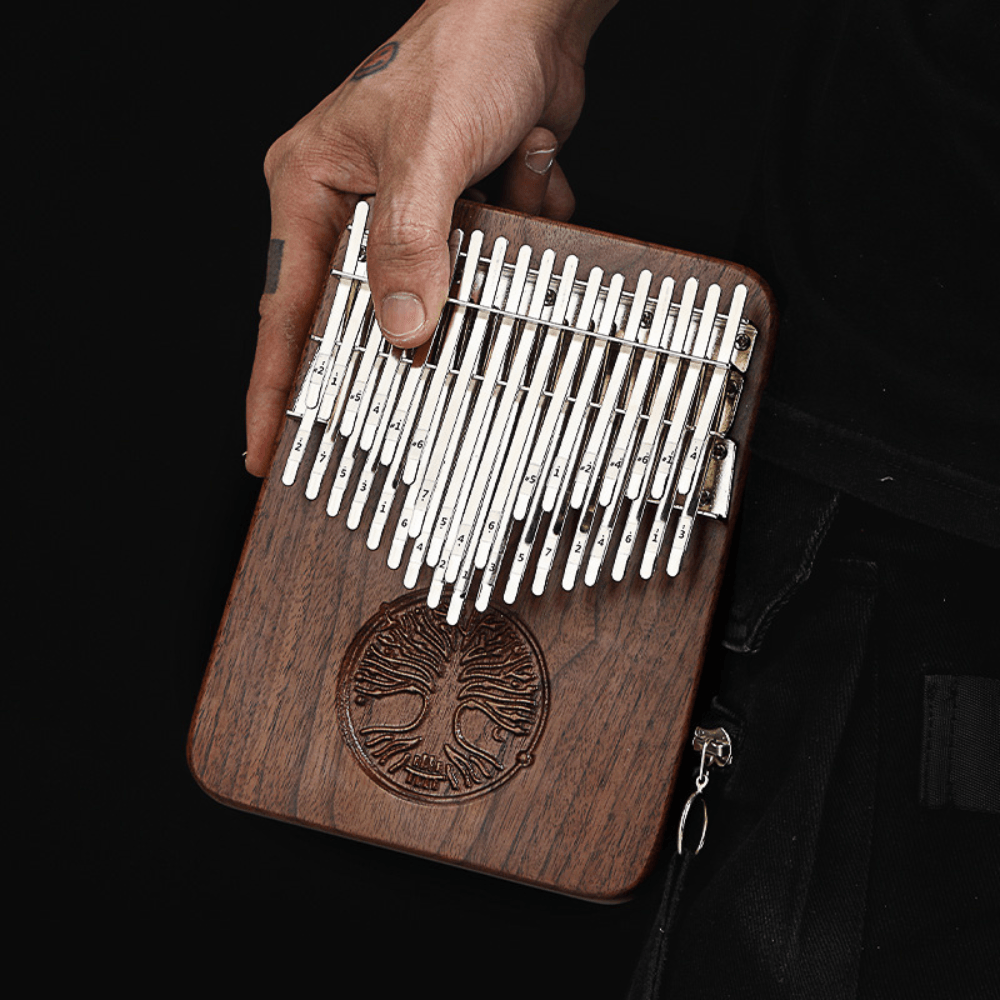 Hand holding wooden kalimba with tree of life carving, metal tines numbered for easy play