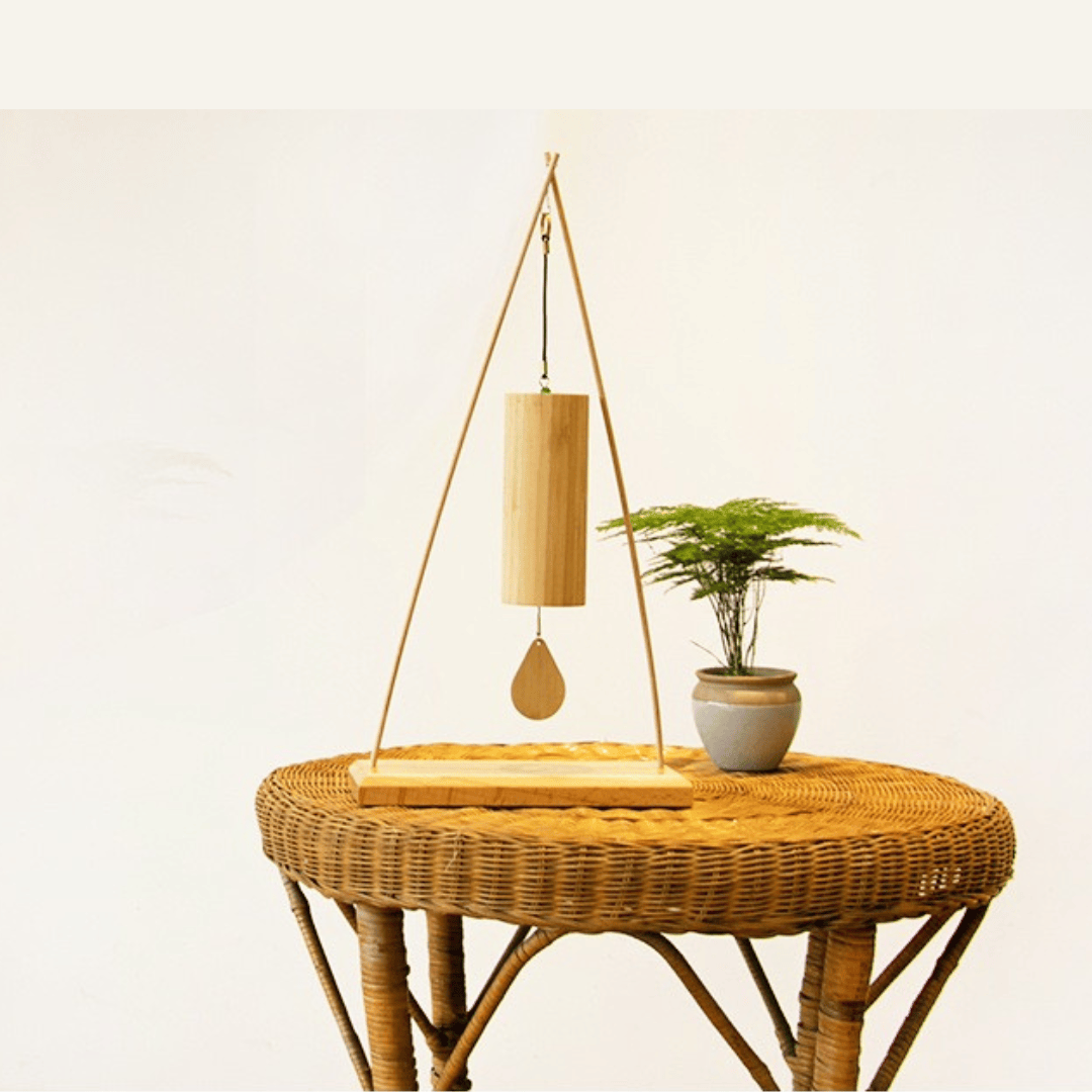 Bamboo wind chime with wooden striker on wicker table, beside potted plant, for serene home ambiance