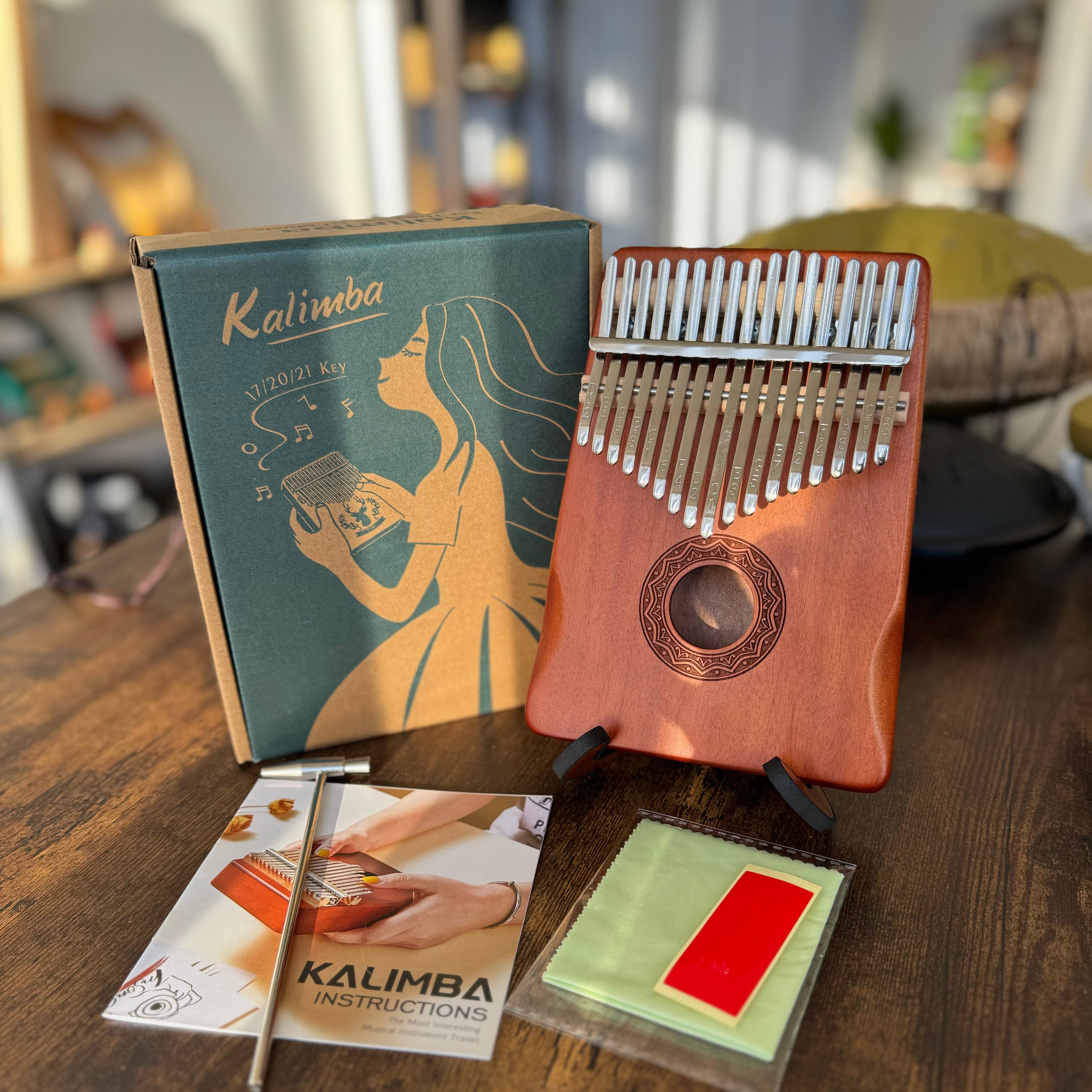 Wooden kalimba thumb piano with 17/20/21 keys, instruction booklet, and cleaning cloth on table
