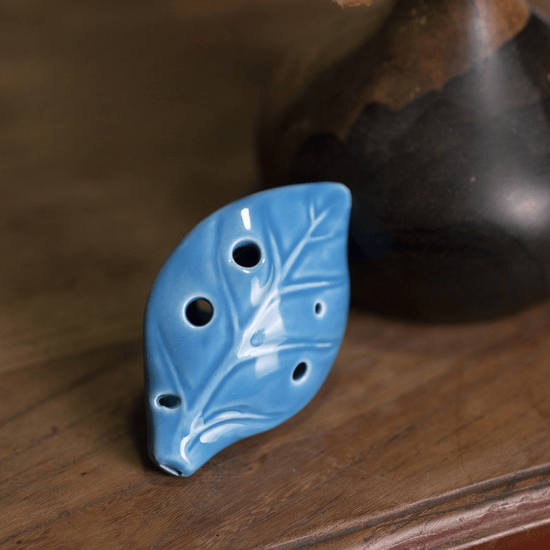 Blue leaf-shaped ceramic ocarina with detailed vein design, resting on wooden surface