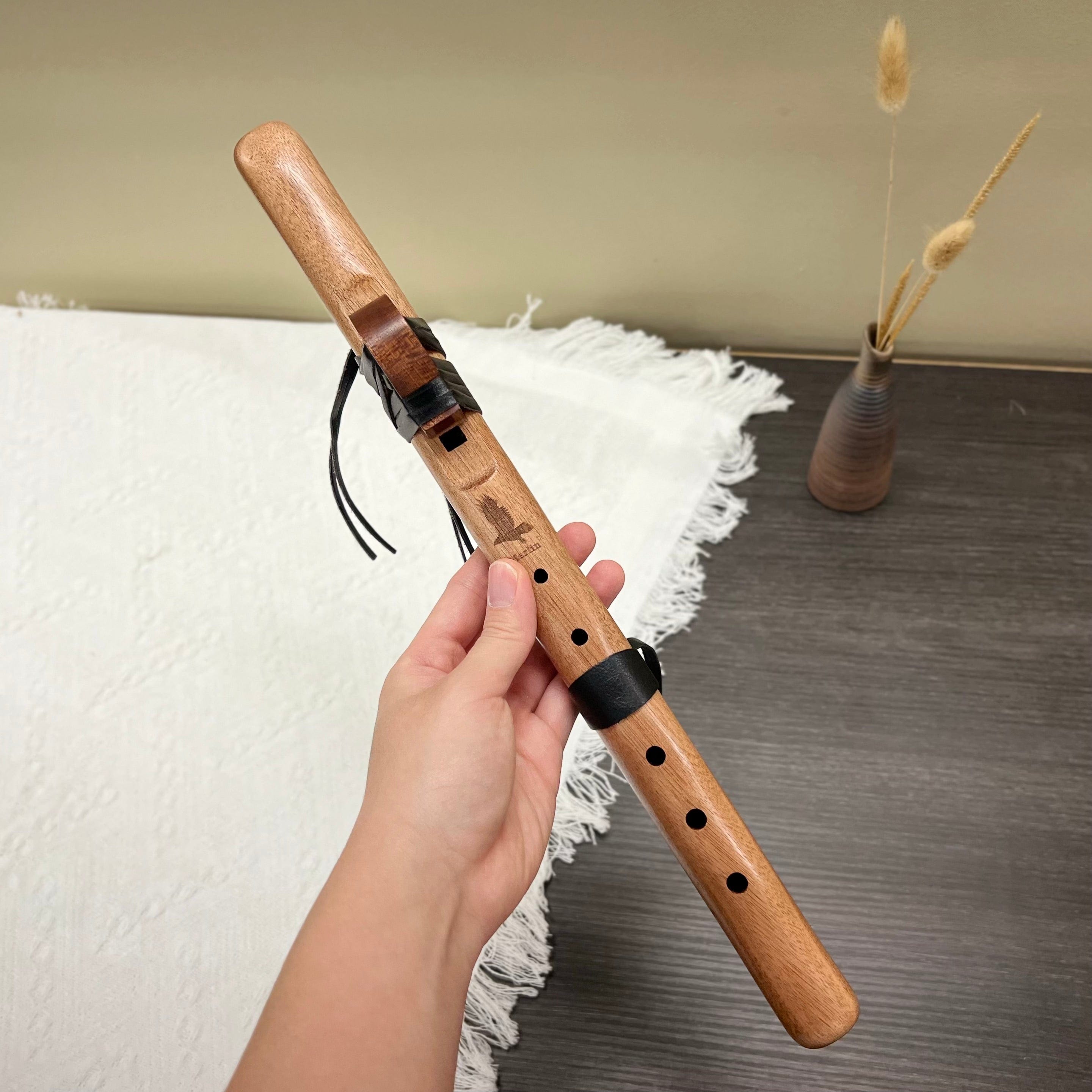 Hand holding wooden flute with leather accents, ideal for healing music and meditation practices.