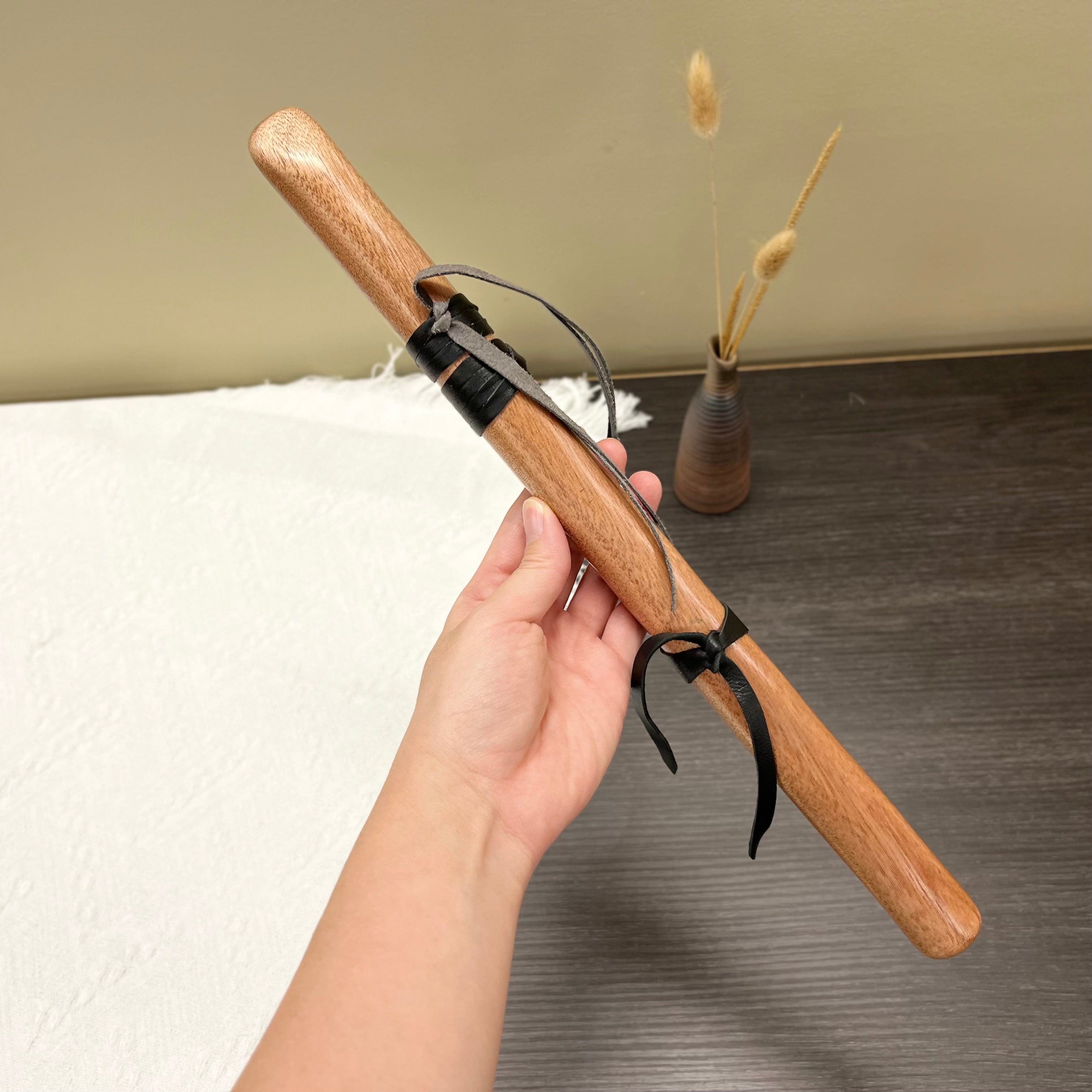 Hand holding wooden tongue drum mallet with leather straps, ideal for healing sound therapy and meditation.