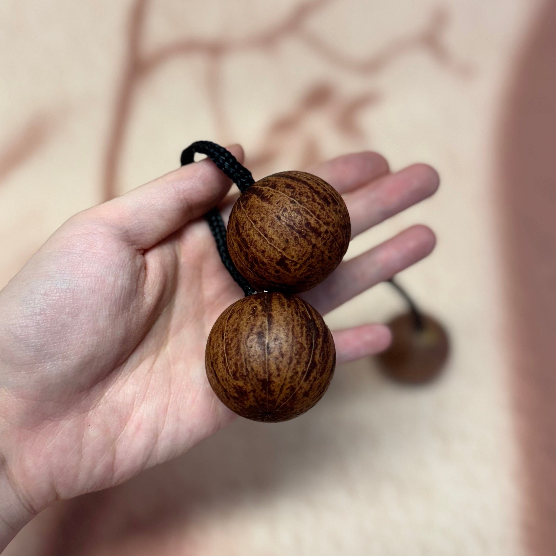 Hand holding two wooden worry balls with black cord, natural texture for stress relief and mindfulness.
