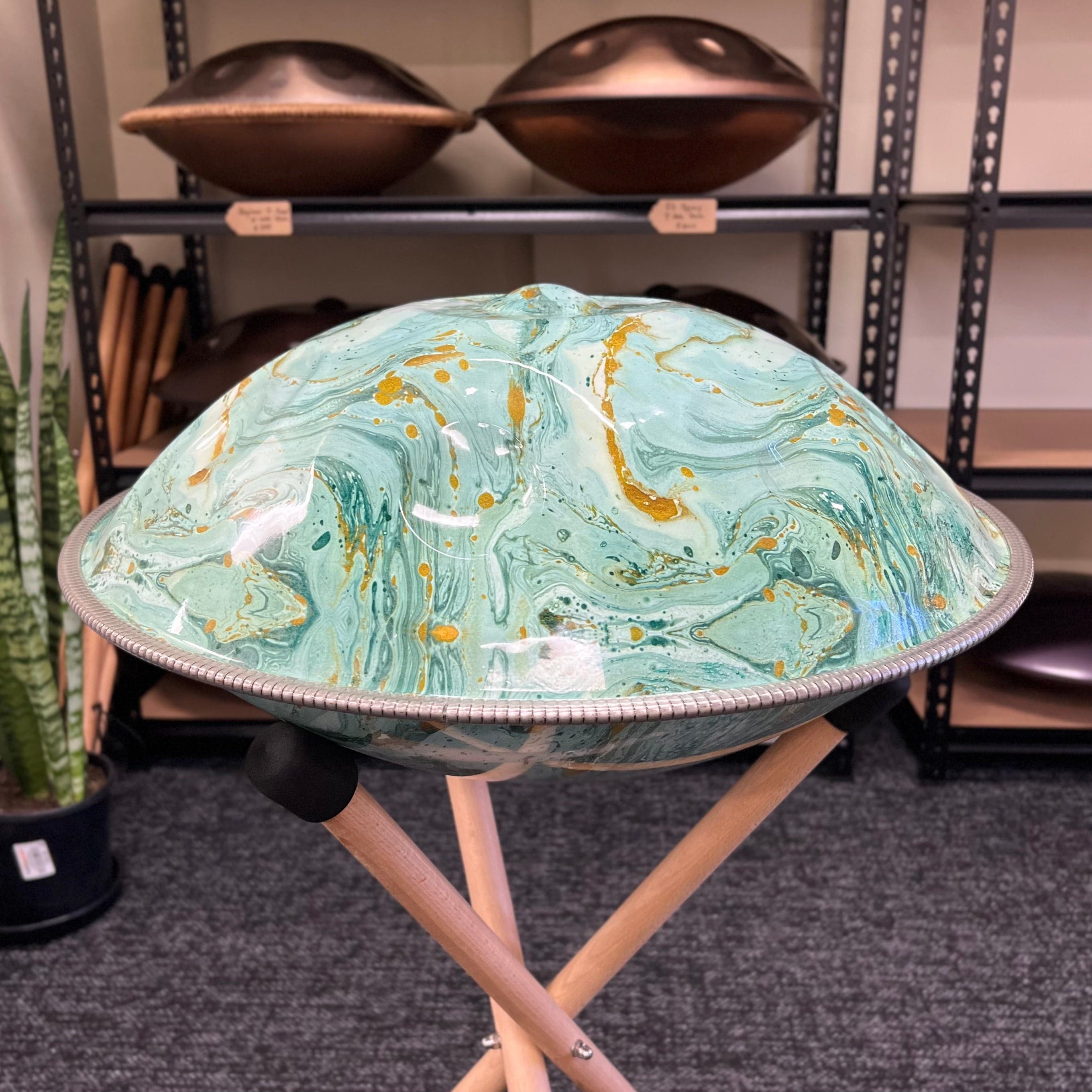Handpan with teal and gold marbled finish on wooden stand, healing musical instrument